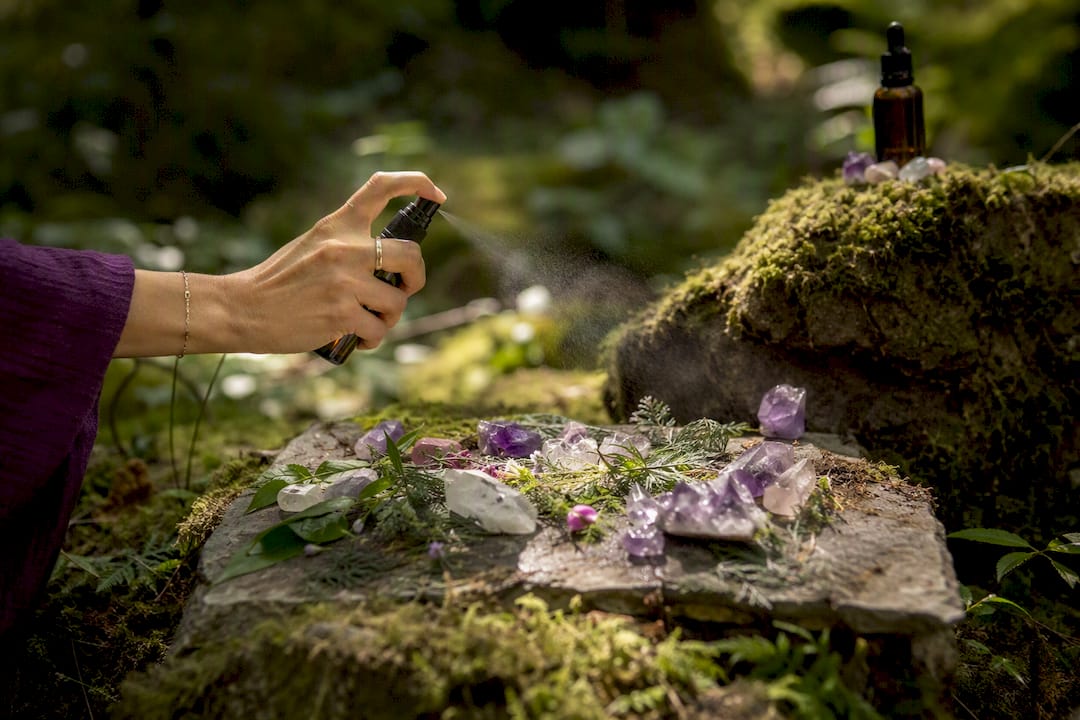 Hand spraying herbal mist over altar with herbs